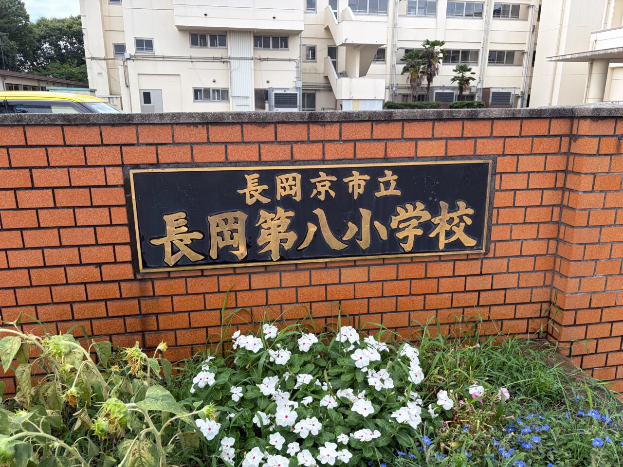 長岡第八小学校のレンガ塀にはめ込まれた校名の銘板と足元の花